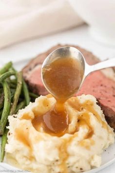 a spoon drizzling sauce over mashed potatoes and green beans on a plate