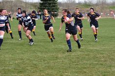 a group of young women playing a game of rugby on a field with trees in the background