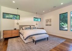 a large bedroom with hardwood floors and white walls, along with two windows that look out onto the woods