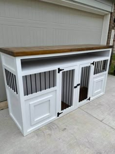 a white dog house with wooden top and doors on the side walk in front of a garage