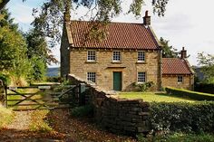 an old stone house with a gate in the foreground and green grass on the other side