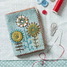 an embroidered book next to some sewing needles and thread on a table with buttons, scissors and needle