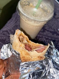 a person holding a half eaten sandwich in front of a drink on a purple table cloth