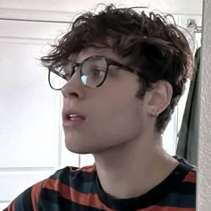 a young man with glasses looking off to the side in front of a mirror and wearing a striped shirt