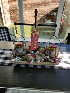 an arrangement of flowers and plants on a table in front of a window with a merry sign