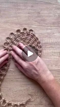 someone is crocheting a chain with their hands on a wooden surface, while another person holds the chain