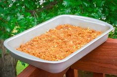 a white dish filled with food sitting on top of a wooden bench next to trees