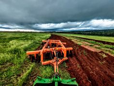 an orange tractor is in the middle of a green field with dark clouds above it