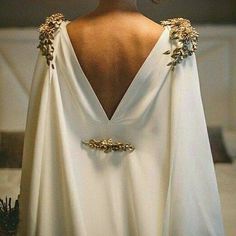 the back of a woman's white dress with gold accents on her neck and shoulders