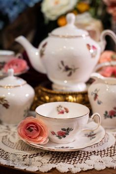 a tea set on a table with pink flowers in the center and white china cups