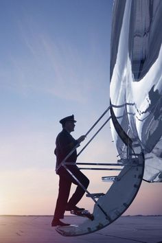 a man standing next to an airplane on top of a tarmac with the sun setting in the background