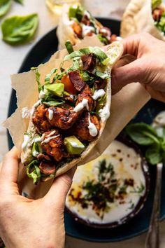 two hands holding up a pita filled with meat and veggies