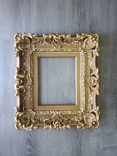 an ornate gold frame hanging on the wall above a wooden table with a gray background