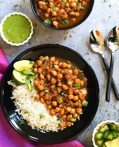 two black bowls filled with chickpeas and rice next to spoons on a table