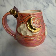 a pink and gold coffee mug sitting on top of a marble countertop next to a white wall