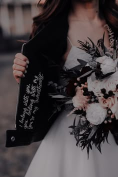 a woman in a white dress holding a black and white bouquet with writing on it