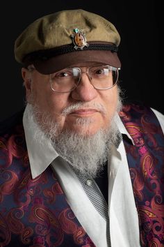 an older man with glasses and a beard wearing a hat is looking at the camera