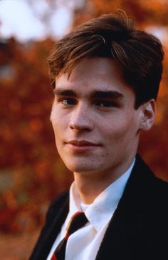 a young man in a suit and tie looking at the camera with trees in the background