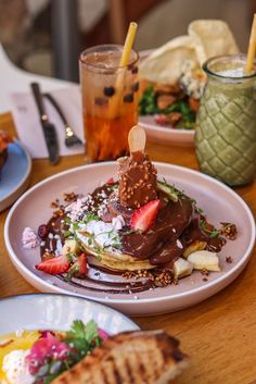 pancakes with chocolate frosting and strawberries are on a plate next to a drink