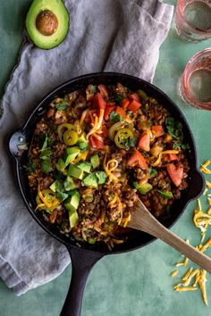 a skillet filled with taco salad next to an avocado and glass of water