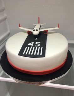 a white and black cake with an airplane on it's top is sitting in a display case