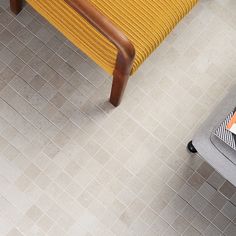 a yellow chair sitting on top of a tiled floor next to a table with an orange blanket