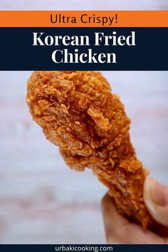 a hand holding up a fried chicken in front of the camera with text overlay reading ultra crispy korean fried chicken