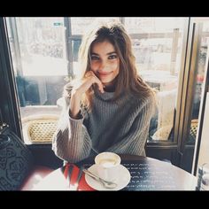 a woman sitting at a table in front of a window with a cup of coffee