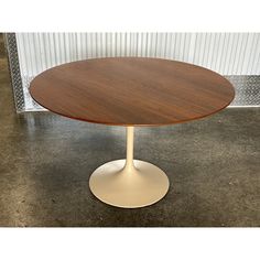 a round wooden table sitting on top of a cement floor next to a white wall