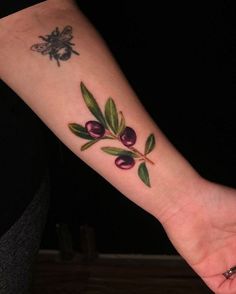 an olive branch tattoo on the left inner forearm and wrist with a bee sitting on it