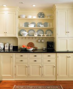 a kitchen with white cabinets and black counter tops, including a bowl of oranges