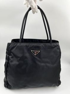 A super cool Prada tote crafted from black nylon, this style is timeless and looks very similar to the current collection. Inside there is a middle zipped compartment plus a further zipped pocket for your valuables. The bag is lined with the iconic Prada logo nylon lining. In overall good condition, with minor signs of wear and some slight marks to the nylon. Please view all photos. Height: 26cm Width: 32cm Depth: 11cm