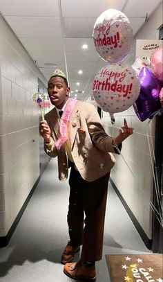 a man in a suit and tie holding balloons with the words happy birthday on them