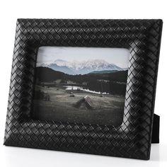 a black photo frame sitting on top of a white table with mountains in the background