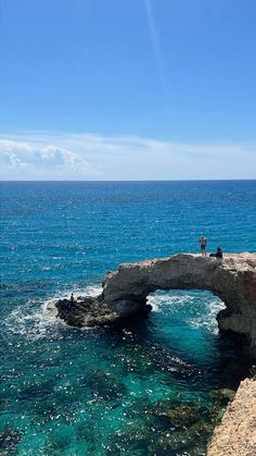 two people standing on the edge of an arch in the ocean