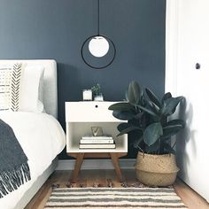 a white bed sitting next to a green plant on top of a wooden floor in a bedroom