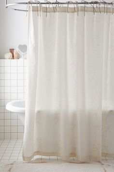 a white shower curtain in a bathroom next to a bathtub and tiled flooring