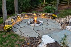 an outdoor fire pit surrounded by rocks and plants with lit candles in the middle on each side