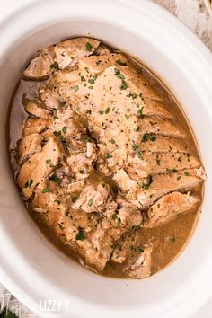 a white bowl filled with meat covered in gravy and garnished with parsley