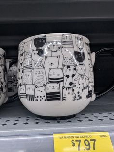 two mugs with cats on them sitting on a shelf in a store display case