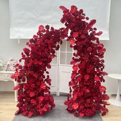 two tall red flowers are in front of a white wall and window with drapes