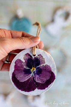 a hand holding a purple flower ornament with twine around it's end