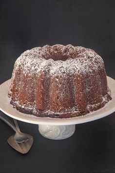 a bundt cake with powdered sugar on top sits on a plate next to a fork