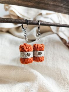 small orange and white crochet earrings hanging from a wooden hook on a bed