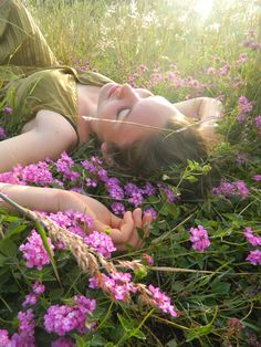 a woman laying in the grass with her eyes closed and hands on her chest, surrounded by purple flowers