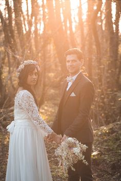 a bride and groom are holding hands in the woods at their wedding day, while the sun shines through the trees behind them