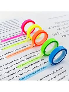 five different colored plastic rings sitting on top of an open book with text in the background