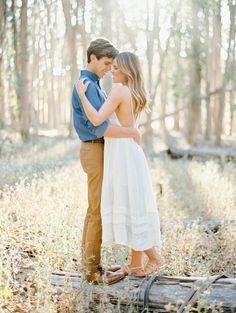 a man and woman standing next to each other on a log in the middle of a forest