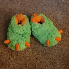 a pair of green slippers with orange feet on carpeted area next to wall