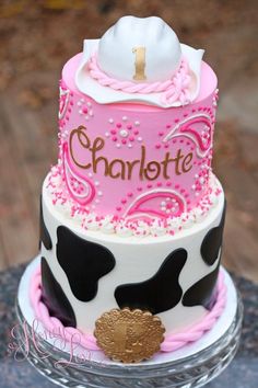 a three tiered cake decorated with pink and black cow print, topped with a white hat